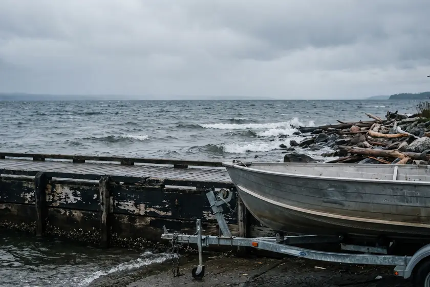 An aluminium fishing boat on a trailer beside a weathered dock on a grey lakeshore